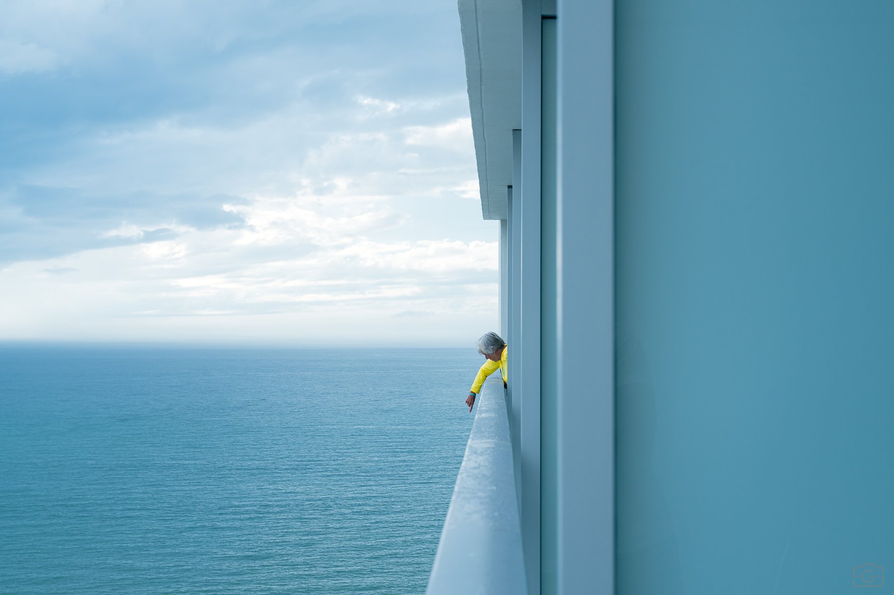 An older woman in yellow pointing down from a balcony above the Gulf